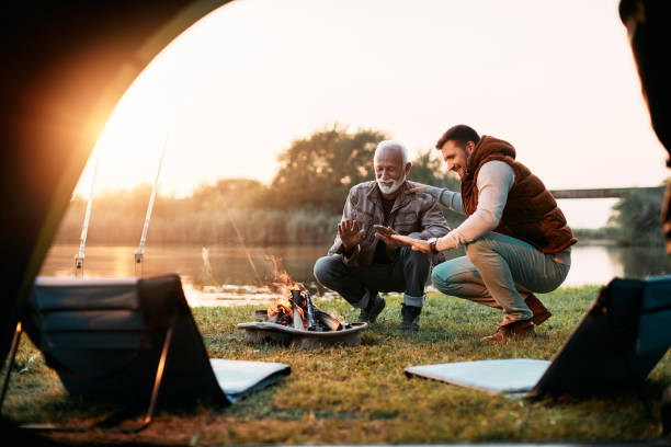 istock Happy senior man and his son warming up by bonfire while camping in nature. 1352400761