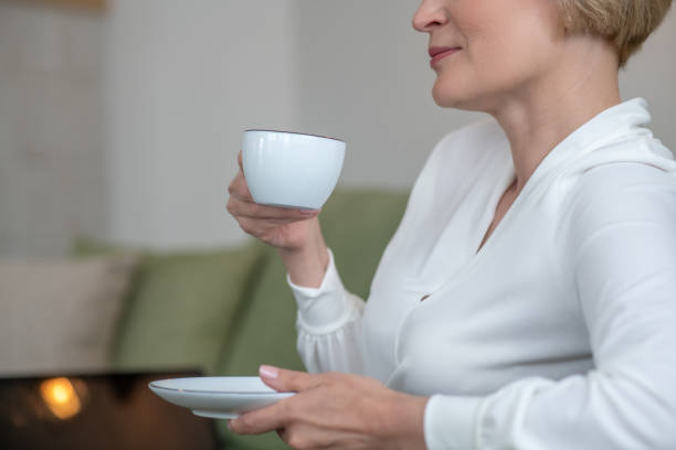 istock Blonde woman sitting on the sofa and having tea 1352410415