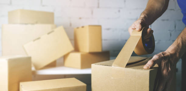 warehouse order picker packing and sealing cardboard box with tape for dispatch