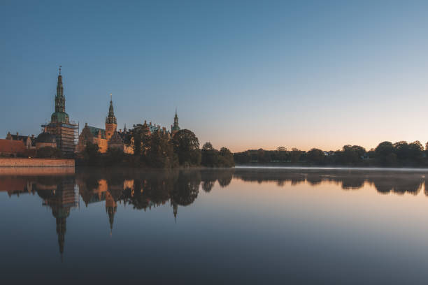 the mirror-shiny lake of Frederiksborg with reflections of the enlightened castle at sunrise stock photo