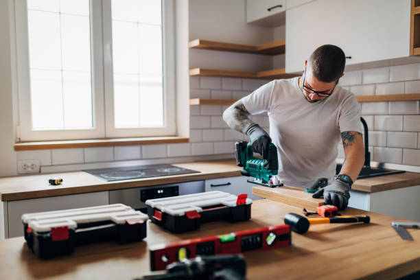 istock Craftsman is using electric jigsaw in the kitchen. On the table in front of him is a tool that he will need for further work. 1352414145