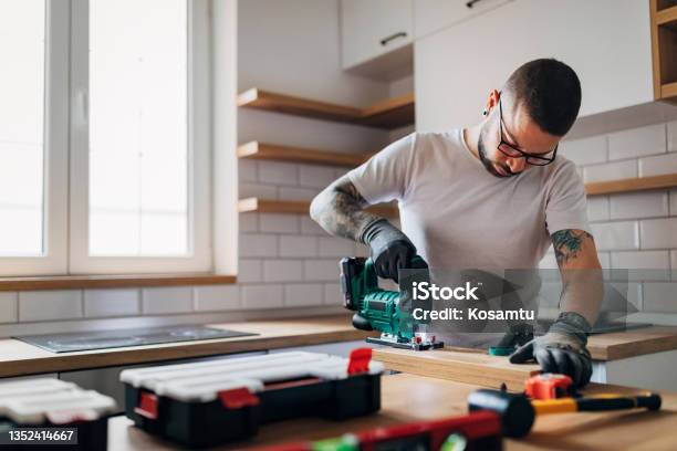 The Bearded Carpenter Using Electric Jigsaw For Cutting A Wooden Plank In His New Kitchen Stock Photo - Download Image Now