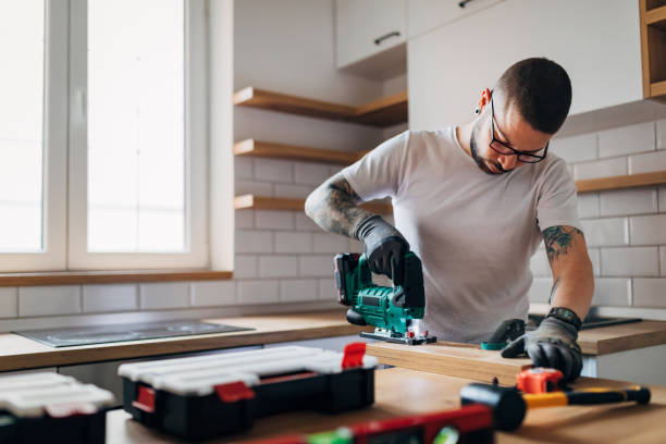 the bearded carpenter using electric jigsaw for cutting a wooden plank in his new kitchen. - home remodeling imagens e fotografias de stock