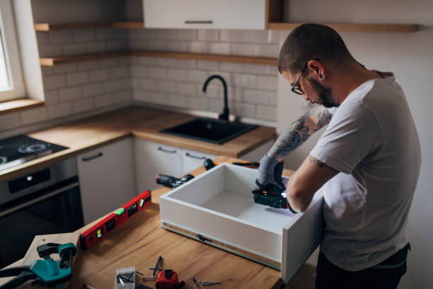 istock Bearded handyman assembling furniture and fixing it. He is in the kitchen and he is using an electric screwdriver. 1352414678