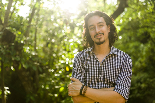 Portrait of big haired white man with beard with checkered shirt among trees, in forest
