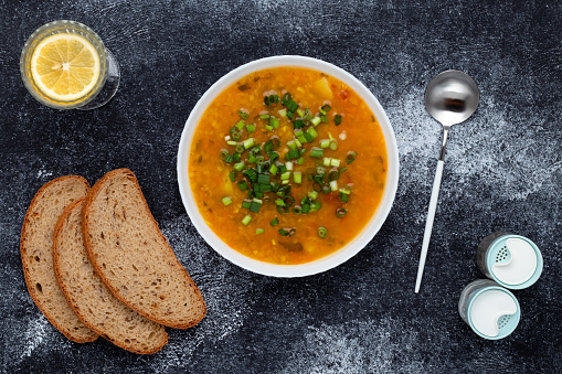 Bowl of vegetarian lentil soup with red lentils and brown bread on dark table. Top view. Food background. A traditional dish of Greek cuisine