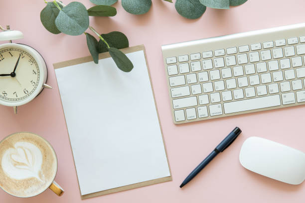 istock pink office desk table with blank paper mockup, alarm clock, keyboard, coffee, pen, eucalyptus leaf, Top view with copy space, flat lay. Pastel. 1352420020