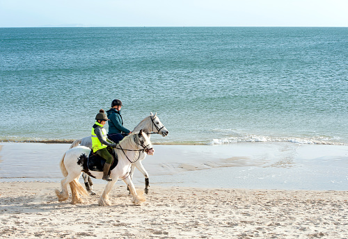 Pair on horseback at Shell Bay near Studland, Dorset, England, UK. A recreational hub on the south coast of England, Poole harbour, the second largest natural harbour in the world, attracts tourists, yachtsmen, hikers and horseriders alike in pursuit of leisure activities along the coastline and water's edge.