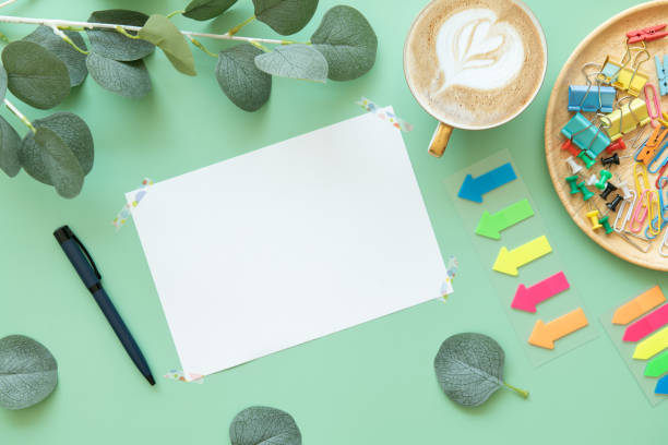 istock green office desk table with blank paper mockup, Paper clip, coffee, pen, eucalyptus leaf, post-it. Top view with copy space, flat lay. Pastel. 1352420470