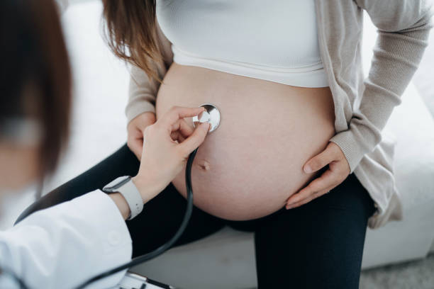 primo piano di una dottoressa che fa un controllo su una donna incinta asiatica, esaminando la pancia con lo stetoscopio. esame prenatale. concetto di salute e benessere della gravidanza - abdomen gynecological examination women loving foto e immagini stock