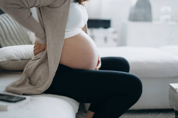 seitenprofil einer schwangeren frau, die ihren bauch berührt und auf dem sofa in einem gemütlichen zuhause sitzt. erwarten sie ein neues leben, wohlbefinden, gesunde schwangerschaft lebensstil - muscular contraction stock-fotos und bilder