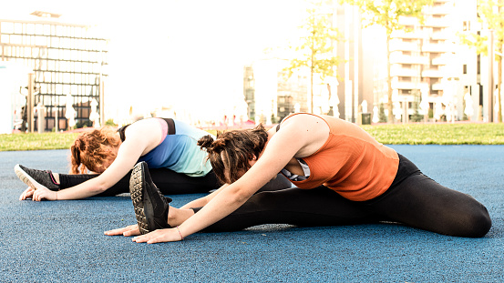 two young women training outdoor, stretching exercise in a public park, wellness and healthy lifestyle concept
