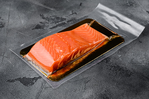 Red fish fillet in vacuum pack set, on gray stone table background, with copy space for text