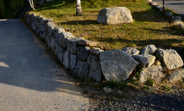 retaining wall of large boulders gray granite by the road around the lawn and asphalt road retaining wall of large boulders gray granite by the road around the lawn and asphalt road boulder rock photos stock pictures, royalty-free photos & images