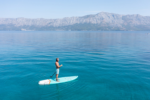 He stands on paddle board and enjoys relaxation on tropical turquoise lagoon