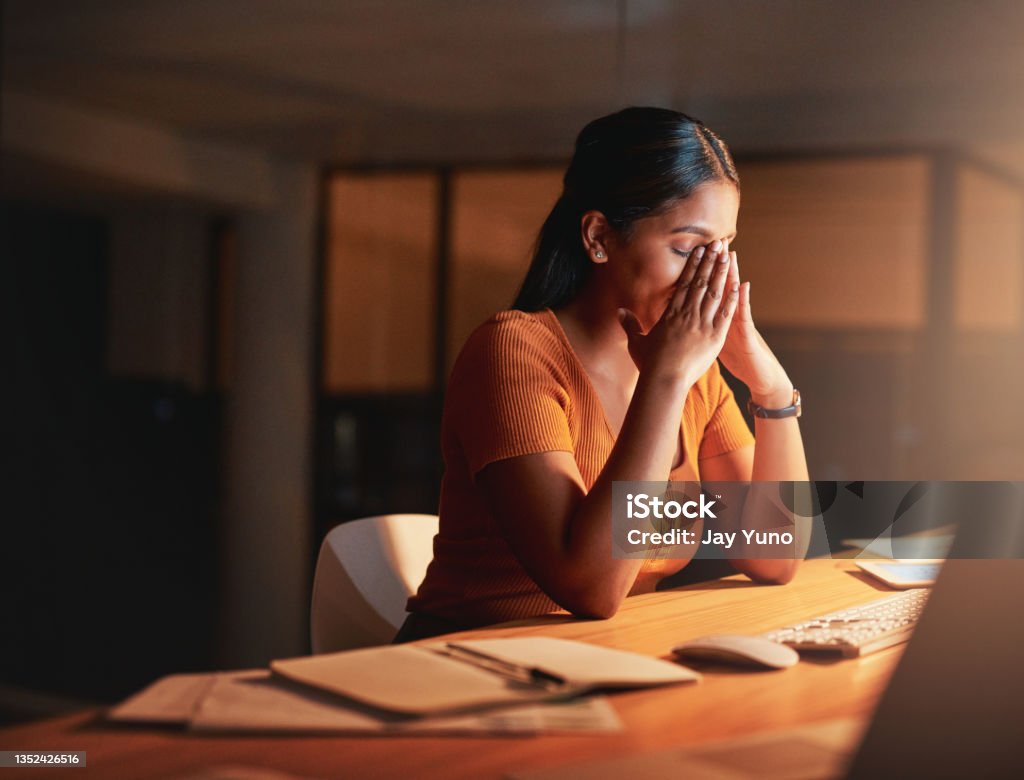 Shot of an attractive young businesswoman sitting alone in the office at night and feeling stressed This stress is something else Emotional Stress Stock Photo