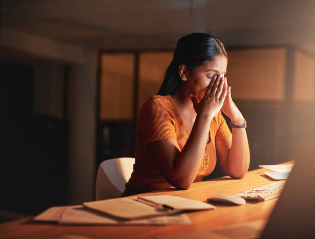 shot of an attractive young businesswoman sitting alone in the office at night and feeling stressed - asian and indian ethnicities imagens e fotografias de stock