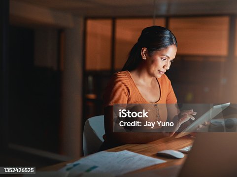 istock Shot of an attractive young businesswoman sitting alone in the office at night and using a digital tablet 1352426525
