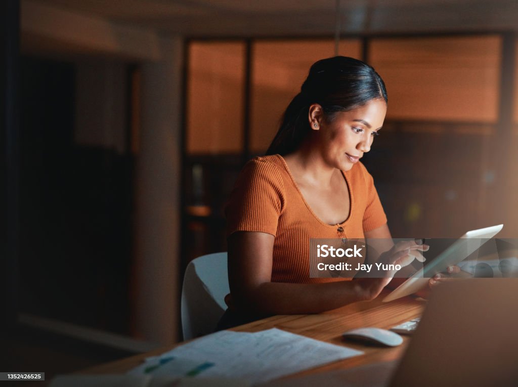 Shot of an attractive young businesswoman sitting alone in the office at night and using a digital tablet Everything seems to be going according to plan Women Stock Photo