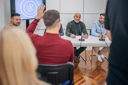 Rear view of a businessman raising his hand to ask a question on a meeting in conference room. Focus is on arm.