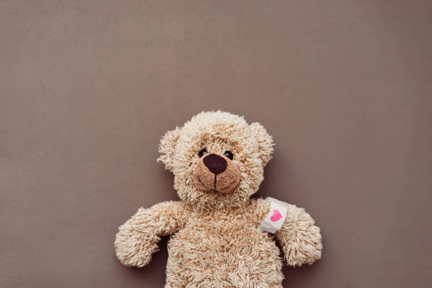a little brown teddy bear with an adhesive bandage and a red heart - speelgoedbeest stockfoto's en -beelden