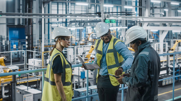 istock Young Diverse Team of Car Factory Engineers in High Visibility Vests Using Laptop Computer. Automotive Industrial Manufacturing Facility Working on Vehicle Production. Diversity on Assembly Plant. 1352428658