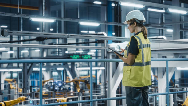 istock Female Car Factory Engineer in High Visibility Vest Using Tablet Computer. Automotive Industrial Manufacturing Facility Working on Vehicle Production with Robotic Technology. Automated Assembly Plant. 1352428685