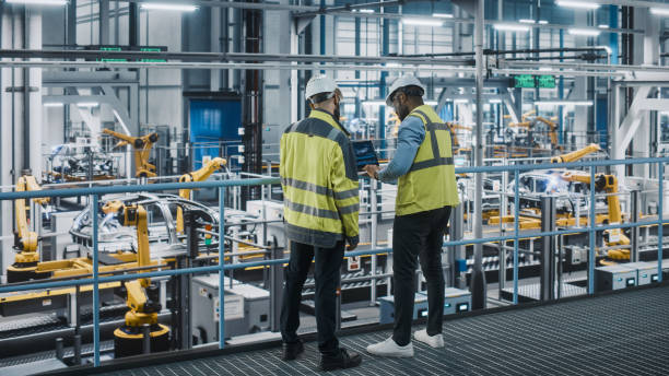 istock Two Car Factory Specialists in High Visibility Vests Using Laptop Computer. Engineers Discussing Automotive Industrial Manufacturing Facility Process of Vehicle Production. Automated Assembly Plant. 1352428691