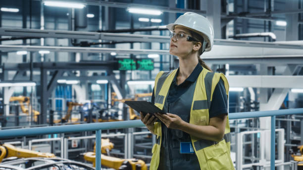 istock Female Car Factory Engineer in High Visibility Vest Using Tablet Computer. Automotive Industrial Manufacturing Facility Working on Vehicle Production with Robotic Technology. Automated Assembly Plant. 1352428704