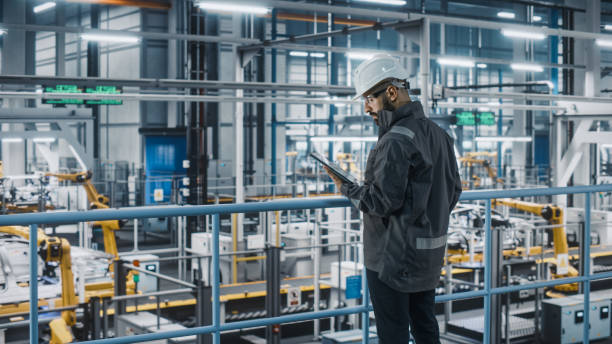 istock Car Factory Engineer in Work Uniform Using Tablet Computer. Automotive Industrial Manufacturing Facility Working on Vehicle Production with Robotic Arms Technology. Automated Assembly Plant. 1352428728