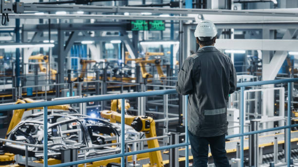 istock Multiethnic Car Factory Engineer in Work Uniform Using Tablet Computer. Automotive Industrial Manufacturing Facility Working on Vehicle Production with Robotic Arms. Automated Assembly Plant. 1352428731