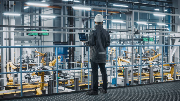 istock Car Factory Engineer in Work Uniform Using Laptop Computer. Automotive Industrial Manufacturing Facility Working on Vehicle Production with Robotic Arms Technology. Automated Assembly Plant. 1352428739