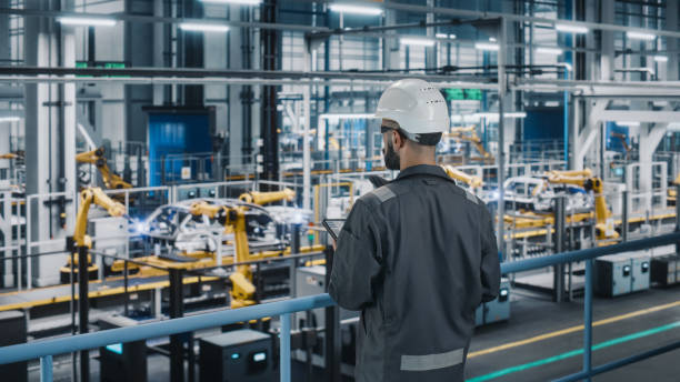 istock Car Factory Engineer in Work Uniform Using Tablet Computer. Automotive Industrial Manufacturing Facility Working on Vehicle Production with Robotic Arms Technology. Automated Assembly Plant. 1352428755
