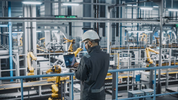istock Car Factory Engineer in Work Uniform Using Laptop Computer. Automotive Industrial Manufacturing Facility Working on Vehicle Production with Robotic Arms Technology. Automated Assembly Plant. 1352428802
