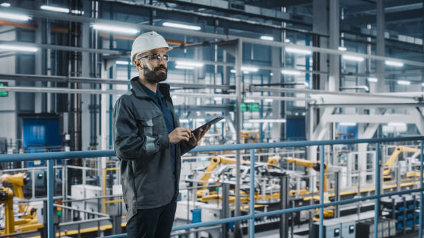 istock Car Factory Engineer in Work Uniform Using Tablet Computer. Automotive Industry 4.0 Manufacturing Facility Working on Vehicle Production with Robotic Arms Technology. Automated Assembly Plant. 1352428826