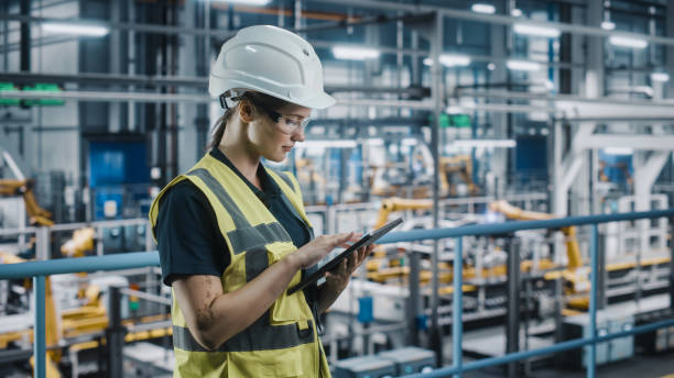 istock Female Car Factory Engineer in High Visibility Vest Using Laptop Computer. Automotive Industrial Manufacturing Facility Working on Vehicle Production with Robotic Arms. Automated Assembly Plant. 1352428849