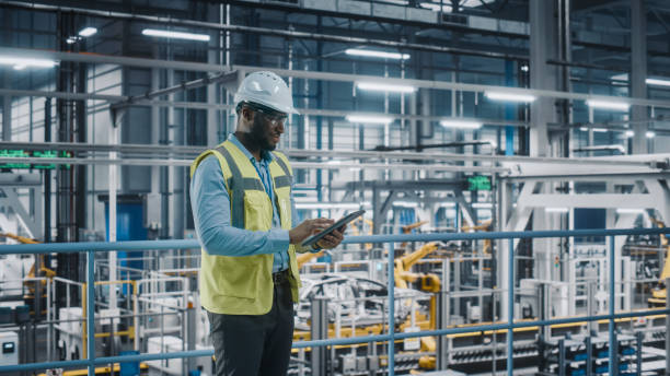 istock Happy African American Car Factory Engineer in High Visibility Vest Using Tablet Computer. Automotive Industrial Facility Working on Vehicle Production on Automated Technology Assembly Plant. 1352428853
