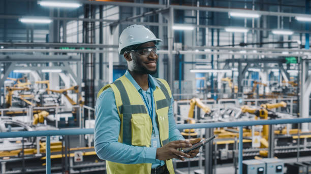 istock Happy African American Car Factory Engineer in High Visibility Vest Using Tablet Computer. Automotive Industrial Facility Working on Vehicle Production on Automated Technology Assembly Plant. 1352428861