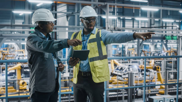istock Multiethnic Manager and African American Car Factory Engineer in Uniform Using Tablet Computer. Automotive Industry 4.0 Manufacture Employees Discuss Work on Vehicle Assembly Plant. 1352428864