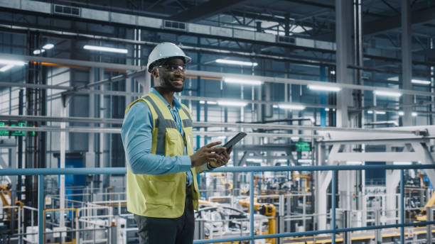 istock Happy African American Car Factory Engineer in High Visibility Vest Using Tablet Computer. Automotive Industrial Facility Working on Vehicle Production on Automated Technology Assembly Plant. 1352428866