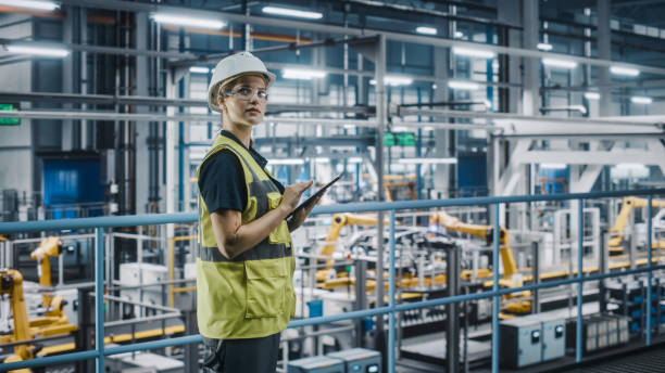 istock Female Car Factory Engineer in High Visibility Vest Using Laptop Computer. Automotive Industrial Manufacturing Facility Working on Vehicle Production with Robotic Arms. Automated Assembly Plant. 1352428875