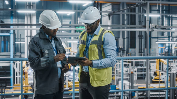 istock Multiethnic Manager and African American Car Factory Engineer in Uniform Using Tablet Computer. Automotive Industry 4.0 Manufacture Employees Discuss Work on Vehicle Assembly Plant. 1352428877