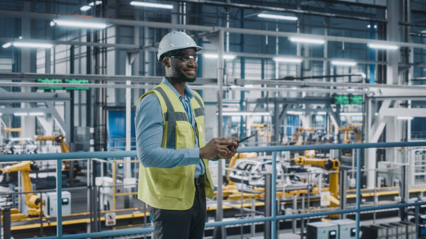 istock Happy African American Car Factory Engineer in High Visibility Vest Using Tablet Computer. Automotive Industrial Facility Working on Vehicle Production on Automated Technology Assembly Plant. 1352428880