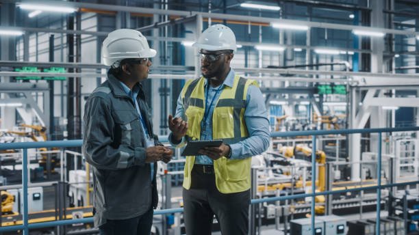 istock Multiethnic Manager and African American Car Factory Engineer in Uniform Using Tablet Computer. Automotive Industry 4.0 Manufacture Employees Discuss Work on Vehicle Assembly Plant. 1352428908