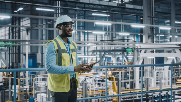 istock Happy African American Car Factory Engineer in High Visibility Vest Using Tablet Computer. Automotive Industrial Facility Working on Vehicle Production on Automated Technology Assembly Plant. 1352428940