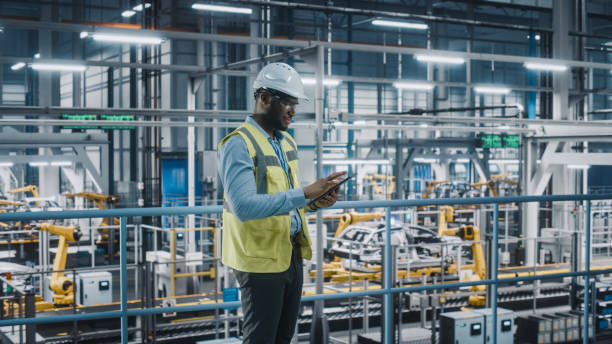 istock Happy African American Car Factory Engineer in High Visibility Vest Using Tablet Computer. Automotive Industrial Facility Working on Vehicle Production on Automated Technology Assembly Plant. 1352428945