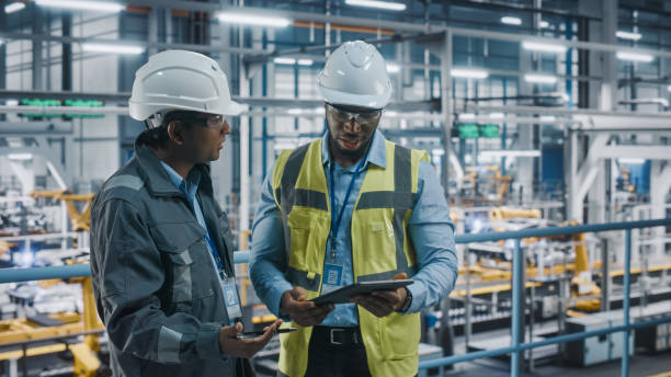 istock Multiethnic Manager and African American Car Factory Engineer in Uniform Using Tablet Computer. Automotive Industry 4.0 Manufacture Employees Discuss Work on Vehicle Assembly Plant. 1352428956