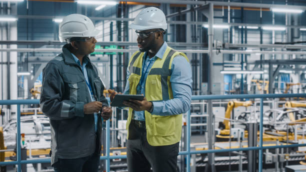 istock Multiethnic Manager and African American Car Factory Engineer in Uniform Using Tablet Computer. Automotive Industry 4.0 Manufacture Employees Discuss Work on Vehicle Assembly Plant. 1352428978