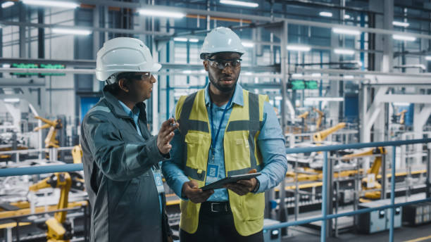 istock Multiethnic Manager and African American Car Factory Engineer in Uniform Using Tablet Computer. Automotive Industry 4.0 Manufacture Employees Discuss Work on Vehicle Assembly Plant. 1352428979