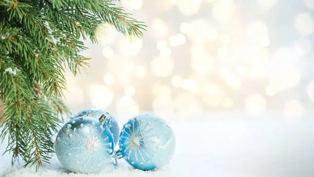 Photo of Light Christmas background blurred, sparkling. Spruce branches and blue Christmas balls in snow on bokeh background. Copy space. Greeting card, happy new year and merry Christmas.